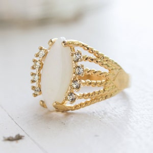 May include: A gold ring with a white oval-shaped stone and clear rhinestones around the stone.
