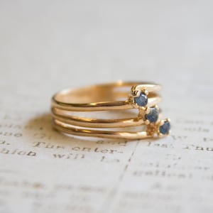 May include: A gold ring with four bands and three blue gemstones. The ring is on a white surface with text.