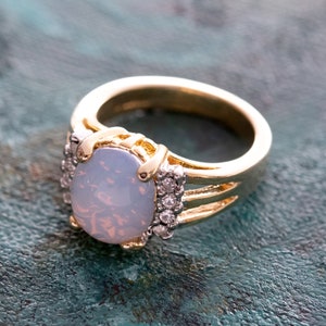 May include: A gold ring with a large oval-shaped opal gemstone and smaller clear gemstones set around the stone.