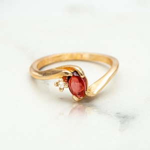 May include: A gold ring with a red gemstone and a small diamond accent.