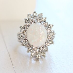 May include: A silver ring with a large white opal stone surrounded by a halo of clear rhinestones.