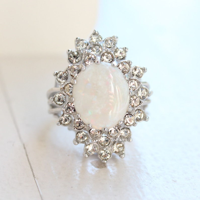 May include: A silver ring with a large white opal stone surrounded by a halo of clear rhinestones.