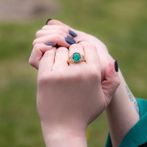 May include: A gold ring with a large oval green gemstone surrounded by smaller clear gemstones.