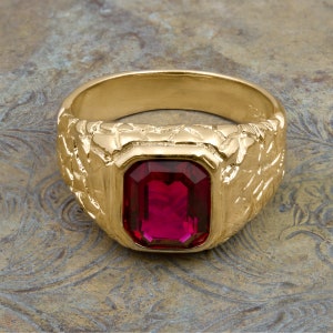 May include: A gold ring with a textured band and a large, rectangular, dark red gemstone.