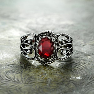 Puede incluir: Un anillo de plata con un diseño adornado que presenta una gran piedra preciosa roja en el centro.
