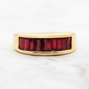 May include: A gold band ring with a row of red baguette-shaped gemstones.