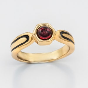 May include: A gold ring with black enamel detailing and a red gemstone in the center.
