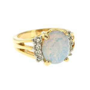 May include: A gold ring with a large oval opal gemstone surrounded by small clear rhinestones. The ring has a delicate, three-band design.