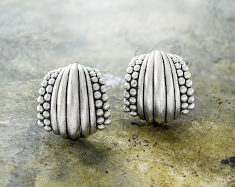 May include: A pair of silver earrings with a textured, ridged design. The earrings are shaped like a half-circle and have a beaded edge.