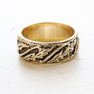 May include: A gold band ring with a detailed, textured design of leaves and vines.
