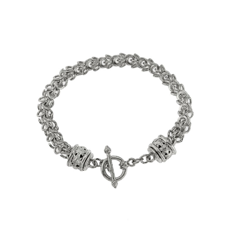 Puede incluir: Una pulsera plateada con cierre de palanca. La pulsera presenta un dise&ntilde;o de cota de malla con cuentas cil&iacute;ndricas decorativas cerca del cierre. El cierre de palanca es de estilo T-bar. La joya se muestra sobre un fondo blanco.