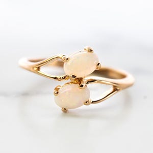 May include: A gold ring featuring two oval white opals. The ring has a delicate, twisted band.