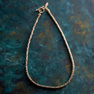 May include: A gold chain necklace with a clasp closure. The chain is made of small, linked squares.