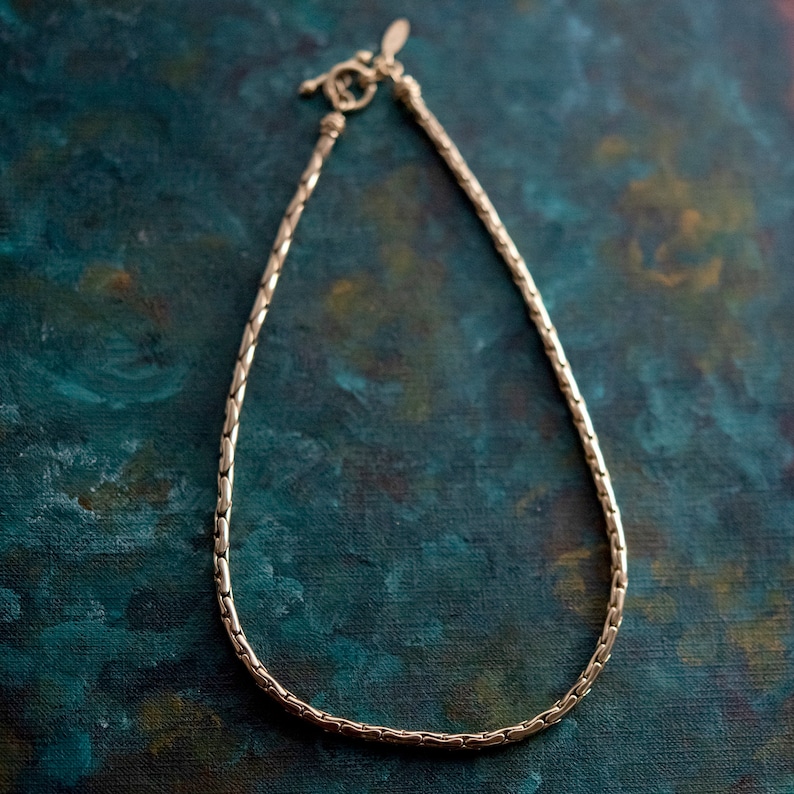 May include: A gold chain necklace with a clasp closure. The chain is made of small, linked squares.