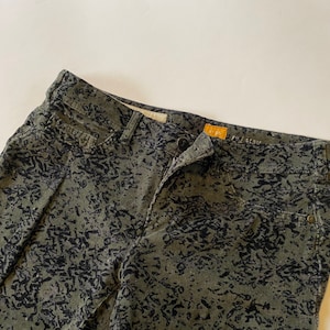 May include: Green corduroy pants with a black abstract print. The pants have a zipper fly and a button closure. The brand name "PILGRIM" is visible on the waistband.