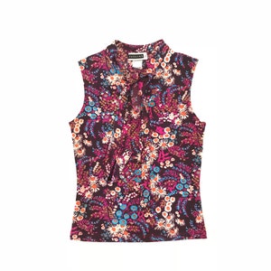 May include: A sleeveless, floral print top with a tie at the neck. The top is a dark brown color with a variety of pink, blue, and white flowers.
