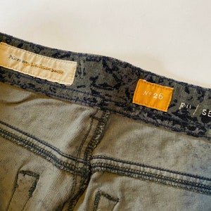May include: Green corduroy pants with a black and white print. The pants have a label that says "Pilgrim Surf + Supply" and another label that says "No. 26".