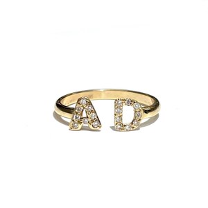 Op de afbeelding: Een gouden ring met twee letters, A en D, bezet met kleine diamanten.