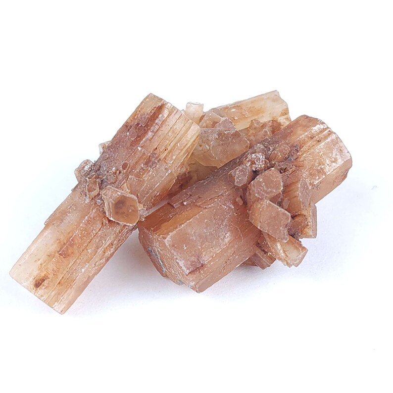 May include: A cluster of aragonite crystals, showcasing a warm, earthy palette of tan and light brown hues. The crystals have a distinct, elongated shape with visible striations, creating a textured appearance. The mineral formation is set against a clean white background.