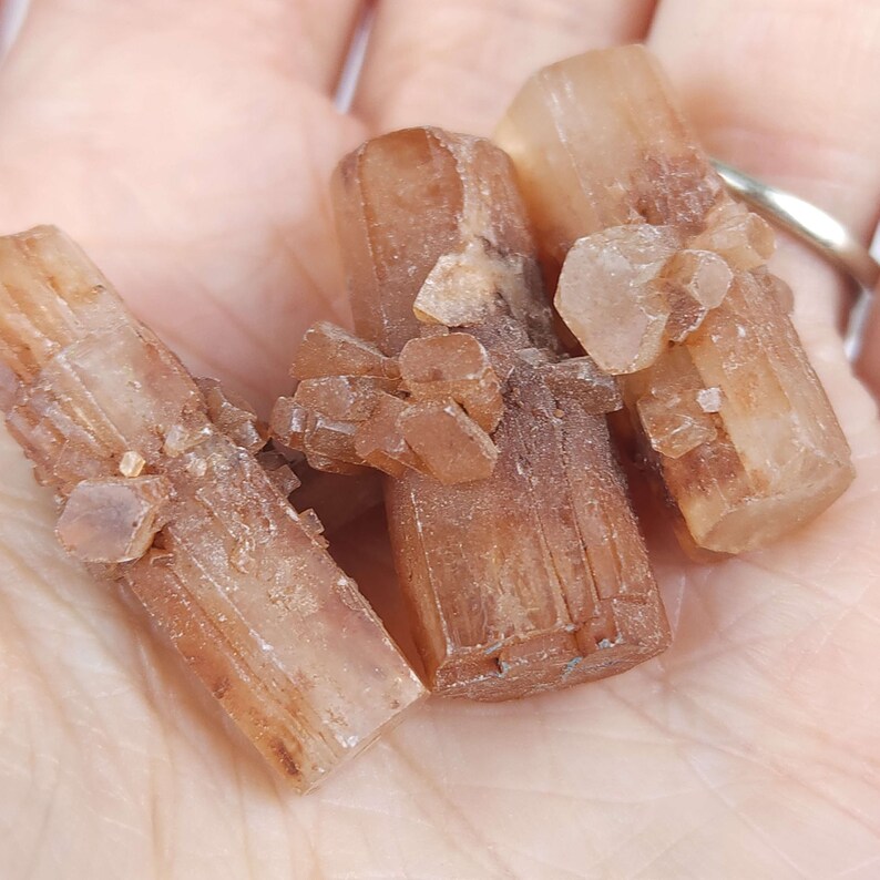 May include: Close-up of several aragonite crystal clusters. The crystals are a warm, earthy brown color with a slightly translucent appearance. The crystals have a natural, rough texture and are clustered together.