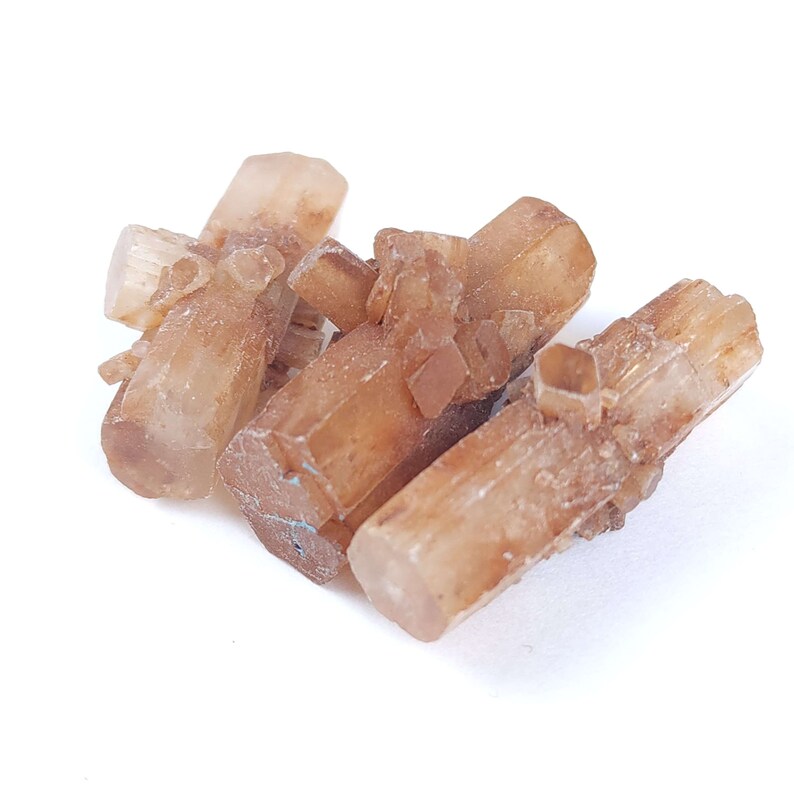 May include: A cluster of aragonite crystals, showcasing a warm, earthy palette of tan and light brown hues. The crystals have a natural, rough texture and are arranged in a visually appealing, clustered formation. The aragonite is set against a clean white background.
