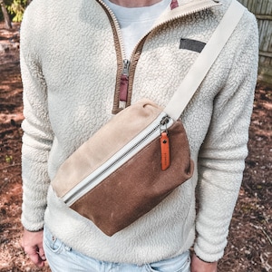 Natural and Tan color block waxed canvas fanny pack with russet leather accents, worn over the shoulder and across the chest.