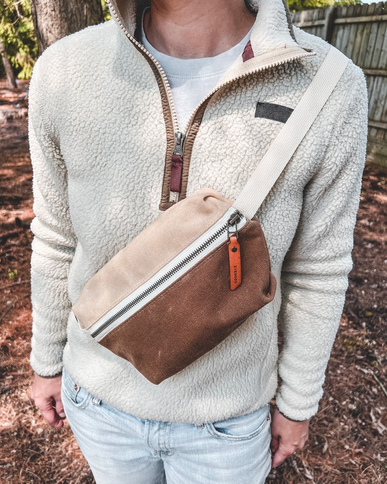 Natural and Tan color block waxed canvas fanny pack with russet leather accents, worn over the shoulder and across the chest.