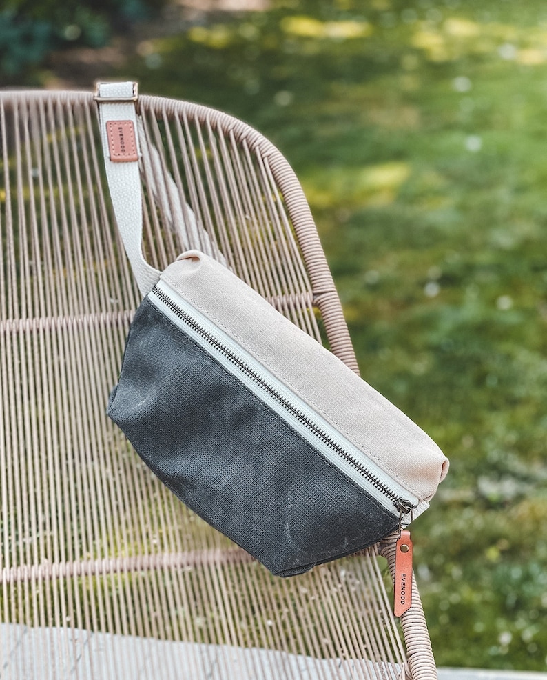 Natural and Charcoal Grey  color block waxed canvas fanny pack with russet leather accents, draped over the back of a chair.