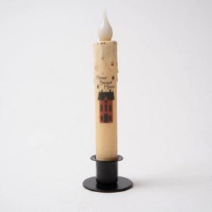May include: A battery-operated candle with a cream-colored wax appearance, featuring a black base. The candle has a printed design of a house and the words "Home Sweet Home." The flame is a bright white LED.