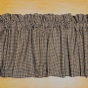 以下が含まれることがあります： 白と黒のギンガムチェックのバランス。生地は上部でギャザーが寄せられ、フリルのような効果を生み出しています。パターンは、キッチンやカントリースタイルの装飾に適した、クラシックなチェックデザインです。