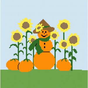 Op de afbeelding: Een glimlachende oranje pompoen-sneeuwpop met een groene sjaal en een bruine hoed staat in een veld met zonnebloemen met oranje pompoenen aan de voet van de zonnebloemen.