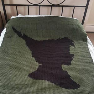 May include: A green crocheted blanket with a black silhouette of Peter Pan.