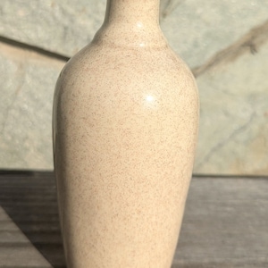 May include: A small, off-white ceramic bottle with a cork stopper. The bottle has a speckled, textured surface.