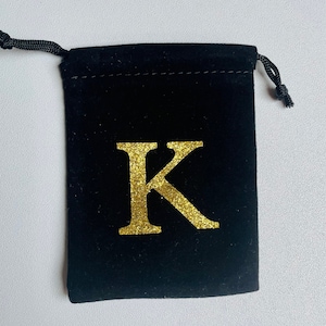 Peut inclure: Pochette en velours noir avec cordon de serrage et une lettre K en paillettes dorées.