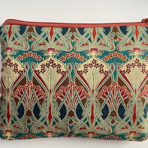 May include: A rectangular zippered pouch with a repeating floral pattern in teal, cream, brown, and burgundy. The pouch has a rust-colored zipper and trim. The design features stylized flowers and leaves, creating a vintage aesthetic. Ideal for carrying small items.