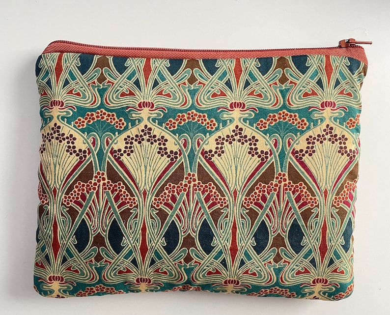 May include: A rectangular zippered pouch with a repeating floral pattern in teal, cream, brown, and burgundy. The pouch has a rust-colored zipper and trim. The design features stylized flowers and leaves, creating a vintage aesthetic. Ideal for carrying small items.