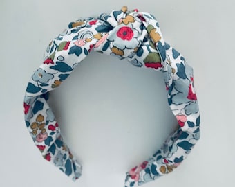 May include: A white headband with a floral pattern in shades of blue, pink, and yellow. The headband is tied in a knot at the top.