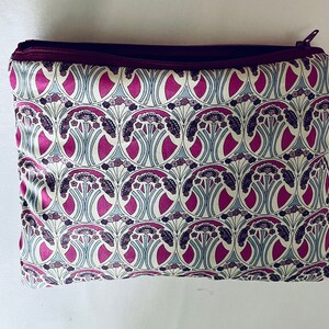 Peut inclure: Une pochette zippée à motif floral rose et blanc. La pochette est en tissu et possède une fermeture éclair bordeaux.