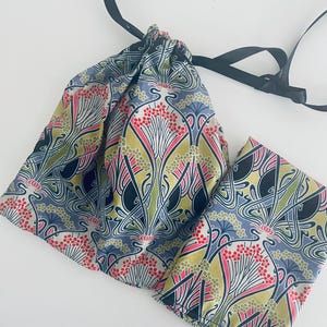 May include: A drawstring bag made of fabric with a floral pattern in shades of blue, green, pink, and black. The bag has a black ribbon tied around it.