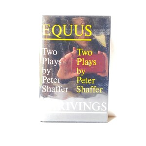 May include: A book cover with the title "Equus: Two Plays by Peter Shaffer" in yellow text on a black background. The cover features a close-up of a person's hand holding a red book.