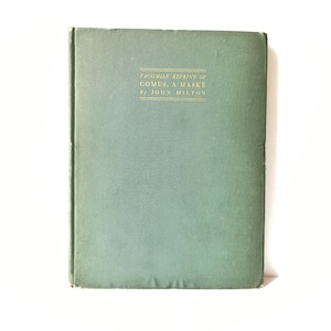 May include: A vintage book with a teal cover. The title "FACSIMILE REPRINT OF COMUS, A MASKE by JOHN MILTON" is printed in gold lettering. The book is closed and set against a white background.