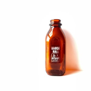 May include: A brown glass milk bottle with a white label that reads "Brock Hall" and a small illustration of a person holding a milk jug.
