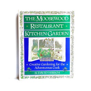 May include: A book titled "The Moosewood Restaurant Kitchen Garden: Creative Gardening for the Adventurous Cook" by David Hirsch. The cover features a blue and green illustration of a window with a garden scene.