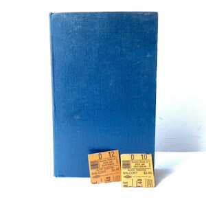 May include: A blue hardcover book with two vintage movie tickets. The tickets are orange with black text, advertising a showing of "Man and Superman" at the Alvin Theatre. The book has a textured cover.
