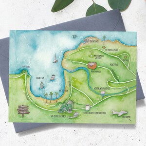 Puede incluir: Impresi&oacute;n art&iacute;stica de mapa en acuarela de una zona costera con tierra verde, agua azul y varios puntos de referencia. El mapa incluye ilustraciones de veleros, surfistas, palmeras y edificios. El mapa est&aacute; en una tarjeta blanca con un sobre gris.