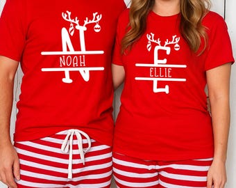 May include: A pair of people wearing matching red t-shirts and red and white striped pyjama bottoms. The t-shirts feature a white reindeer design and a name. The text on the shirts reads "NOAH" and "ELLIE".
