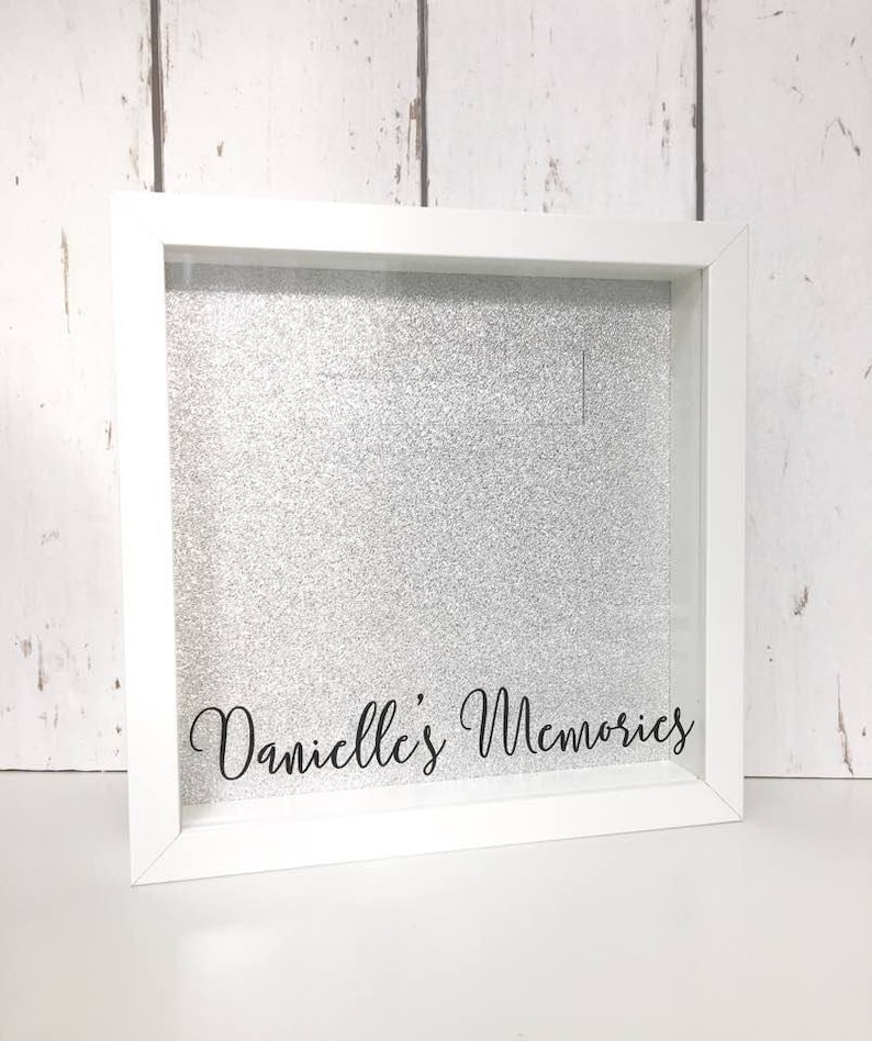 May include: White shadow box with a silver glitter background and the text "Danielle's Memories" in black lettering.