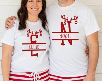 May include: Two people wearing matching white t-shirts with red reindeer designs and names, paired with red and white striped pyjama bottoms. The shirts display the names "Ellie" and "Noah", ideal for Christmas.