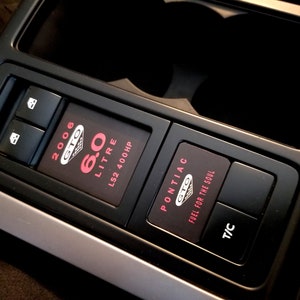 May include: Close-up of a black car interior with a 2006 Pontiac GTO 6.0 Litre LS2 400 HP emblem, a fuel for the soul button, and a T/C button.