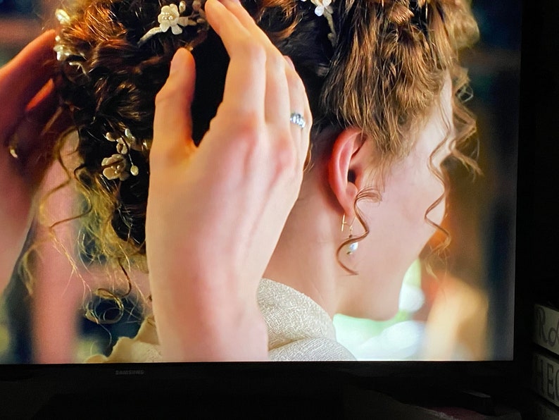 May include: A woman with curly brown hair is having her hair styled. She is wearing a white dress and has a pearl earring in her left ear. Her hair is decorated with a floral hairpiece.